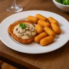 Everyday 26,5 cm-es fehér temperált üveg lapostányéron sertésszelet gombamártással és krokettel, otthonos magyaros bisztróhangulatban, természetes meleg fényekkel.