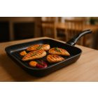 Bio Stone 28x28 cm-es grill serpenyőben aranybarnára pirult csirkemellfilék rozmaringággal és grillezett zöldségekkel, természetes fényű modern konyhai környezetben.