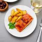 „Basic fehér porcelán tányér mediterrán hangulatban, grillezett hallal és citrommal, naplementés teraszon.”