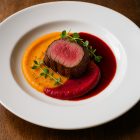 Alaszka fehér porcelán lapostányéron sous-vide marhaszűz sütőtökpürével, céklazselével és mikrozöldekkel, színes fine dining tálalásban