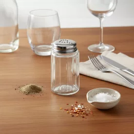 Üveg fűszerszóró rozsdamentes tetővel, őrölt borssal és tengeri sóval, konyhai munkafelületen, evőeszközökkel