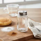 Üveg fűszerszóró porcukorral és fahéjjal, desszert tálalási környezetben, letisztult konyhai stílusban