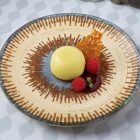 Infinity Micenas porcelán tányéron tálalt pisztáciás fehércsokoládé mousse málnával, karamellropogóssal és málnazselével – fine dining desszert tálalás